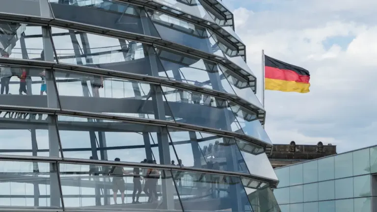 Die gläserne Kuppel des Reichstagsgebäudes mit der wehenden deutschen Flagge im Hintergrund.