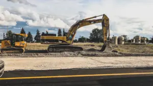 Gelber Bagger bei Erdarbeiten direkt neben einer frisch asphaltierten Straße.