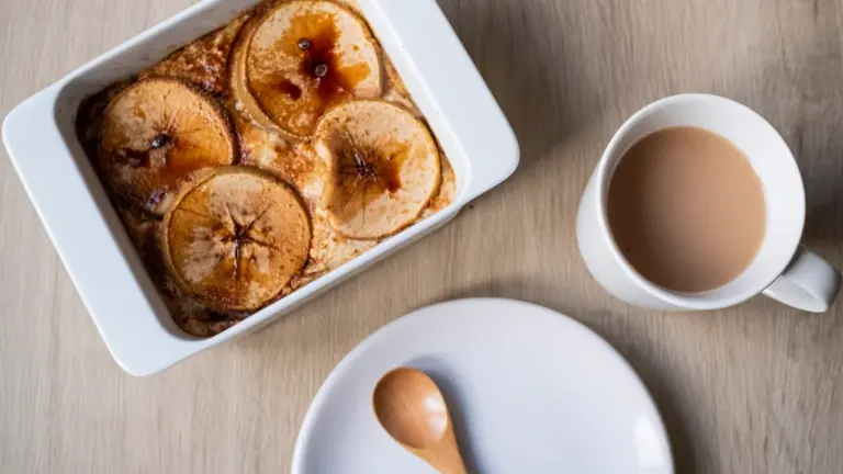 Ein ofenfrischer Apfel-Hafer-Auflauf in einer weißen Auflaufform neben einer Tasse Kaffee