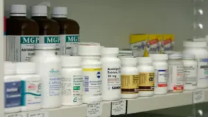 Ein Apothekenregal gefüllt mit verschiedenen Medikamentendosen und Arzneiflaschen im Hintergrund.