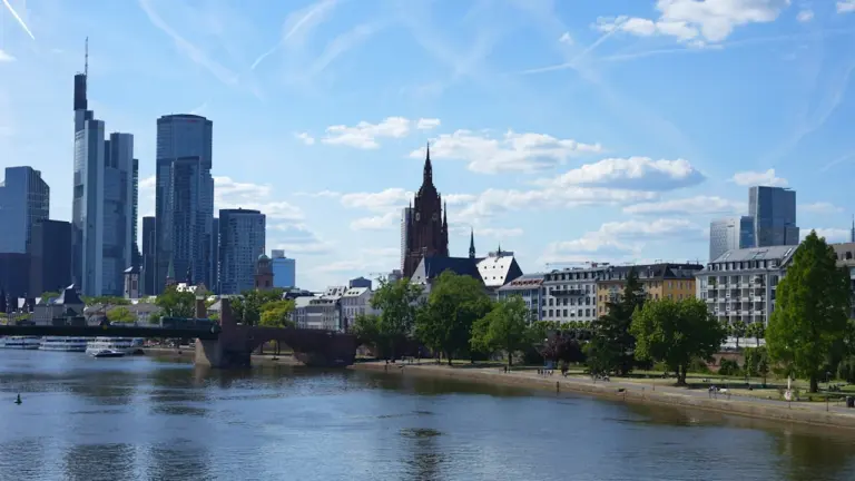 Blick auf die Frankfurter Skyline bei strahlendem Sonnenschein und blauem Himmel über dem Main.