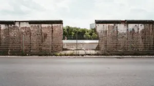 Ein Blick auf einen Abschnitt der Berliner Mauer mit durchgehendem Zaun im Vordergrund.