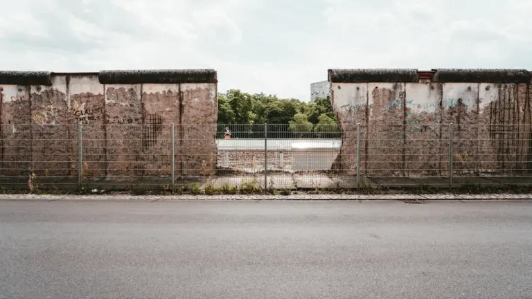Ein Blick auf einen Abschnitt der Berliner Mauer mit durchgehendem Zaun im Vordergrund.