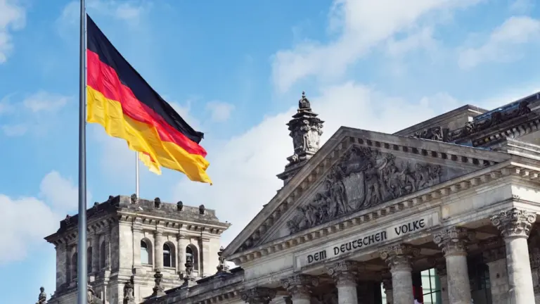 Die deutsche Flagge weht vor dem Berliner Reichstagsgebäude bei blauem Himmel.