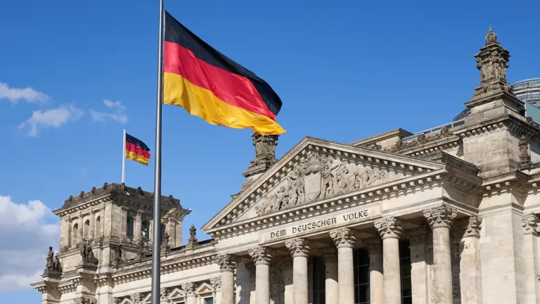 Deutscher Reichstag in Berlin mit wehender deutscher Flagge bei blauem Himmel.