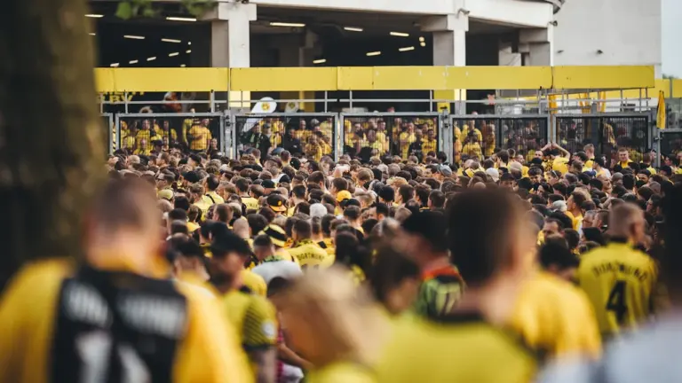Zahlreiche Fußballfans in gelben Trikots warten gespannt vor einem großen Stadiongebäude in Deutschland.