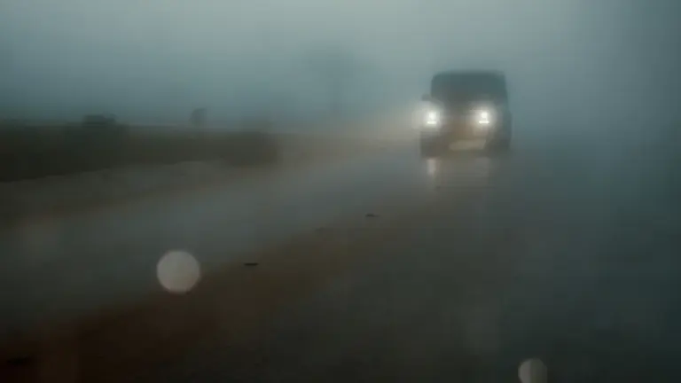 Ein Auto fährt bei starkem Nebel auf einer nassen Landstraße.