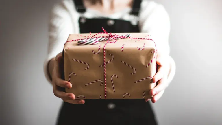 Person hält ein mit Zuckerstangen-Muster verpacktes Geschenk in den Händen.
