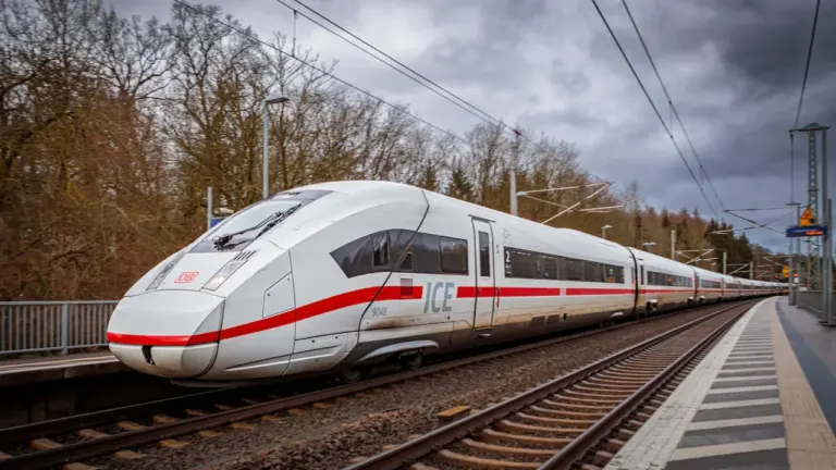 ICE-Zug fährt auf Gleisen durch eine bewaldete Landschaft in Deutschland.