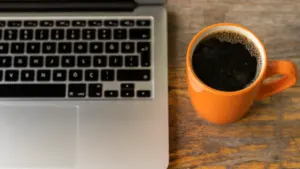 Ein Laptop und eine Tasse Kaffee auf einem Holztisch am Arbeitsplatz.