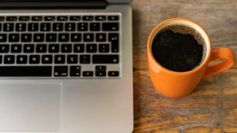 Ein Laptop und eine Tasse Kaffee auf einem Holztisch am Arbeitsplatz.