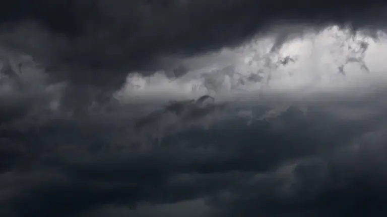 Dunkle, bedrohliche Gewitterwolken ziehen sich dicht am bewölkten Himmel über eine weite Landschaft zusammen.