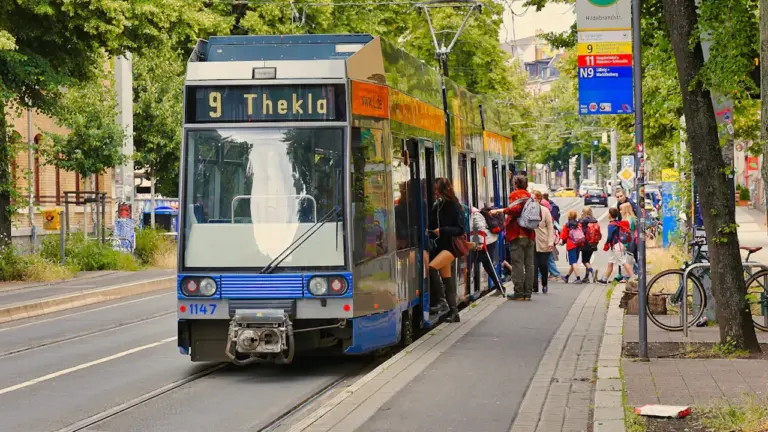 Menschen steigen an einer sonnigen Leipziger Straßenbahnhaltestelle in die Bahn ein.