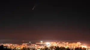 Ein Komet leuchtet hell über einer beleuchteten Stadt bei nächtlicher Dunkelheit.