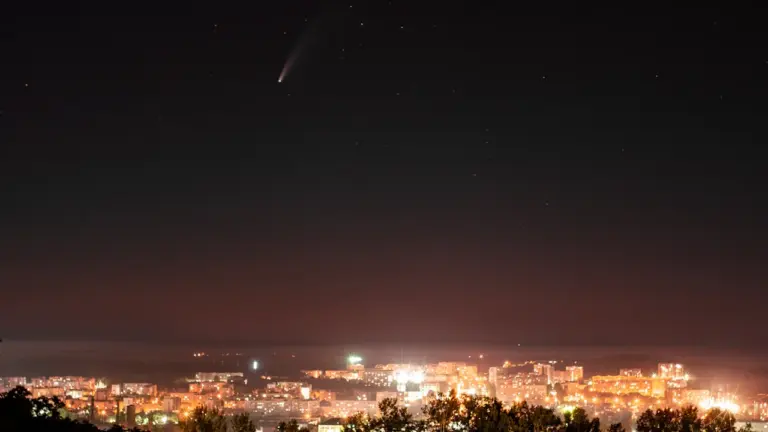 Ein Komet leuchtet hell über einer beleuchteten Stadt bei nächtlicher Dunkelheit.