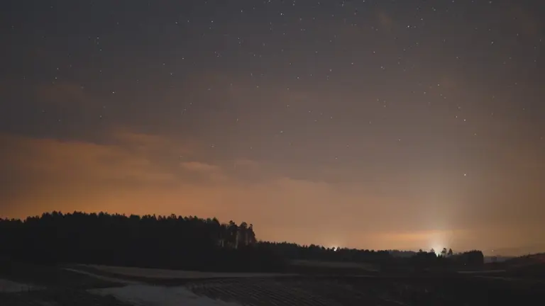 Sternenhimmel über einer deutschen Felderlandschaft mit Baum-Silhouetten in der Dämmerung.