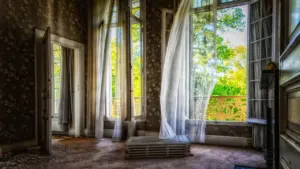 Weißer Fenstervorhang weht sanft durch ein offenes Fenster in einer Wohnung.