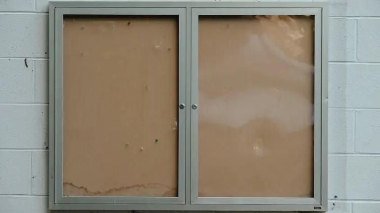 Ein leerer gläserner Aushangkasten an einer weißen Ziegelwand in einer deutschen Stadt.