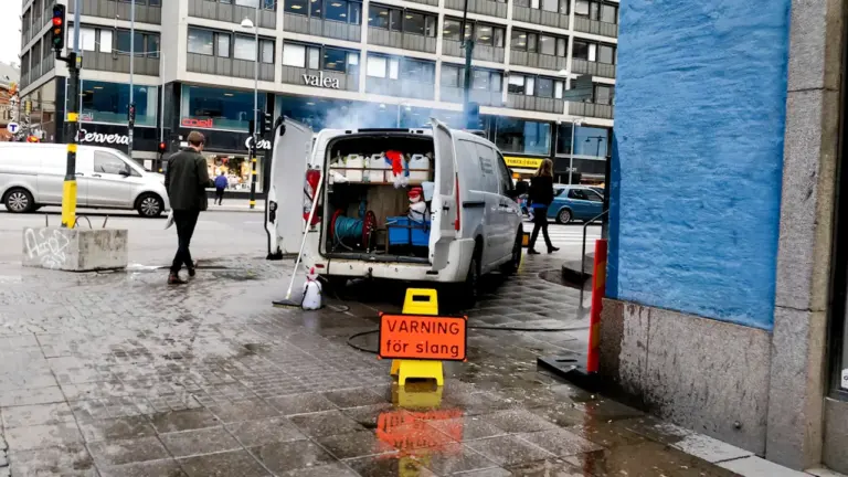 Ein weißer Lieferwagen mit offenem Heck steht auf einer städtischen Straße mit Warnschild.
