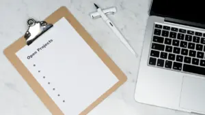 Eine leere Projektliste auf einem Klemmbrett neben einem modernen Laptop auf Marmortisch.