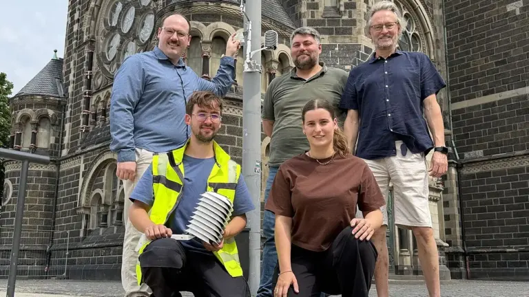 Eine Gruppe von fünf Personen posiert vor einer historischen Kirche mit technischen Messgeräten.
