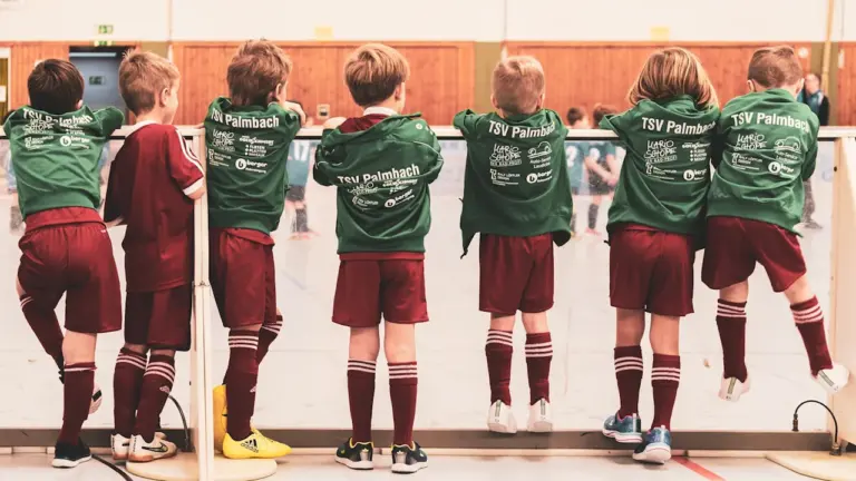 Kinder in Sporttrikots stehen bei einem lokalen Fußballturnier gemeinsam an der Bande.