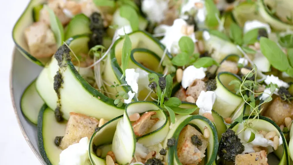 Nahaufnahme eines sommerlichen Zucchini-Salats mit Feta, Pinienkernen und frischen Kräutern auf einem Teller.