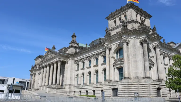 Das historische Reichstagsgebäude in Berlin unter blauem Himmel mit deutscher Flagge.