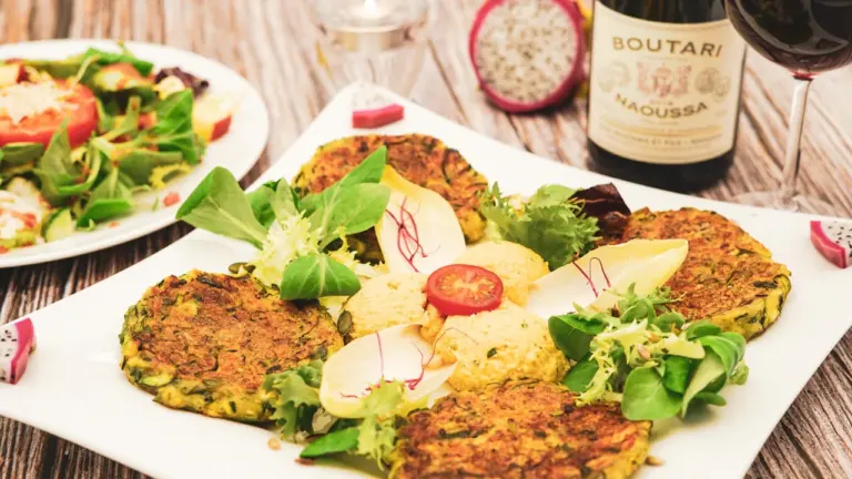 Frische Zucchinipuffer mit Salat und Hummus serviert auf einem weißen Teller