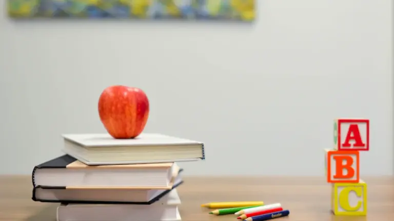 Ein roter Apfel auf einem Stapel Schulbücher neben ABC-Bausteinen auf einem Holztisch.