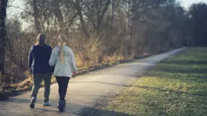 Zwei Personen gehen gemeinsam einen asphaltierten Weg entlang eines Parks in München.