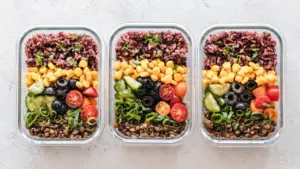 Drei Glasbehälter gefüllt mit gesundem Meal-Prep-Essen auf einem hellen Untergrund.