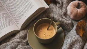 Eine gemütliche Tasse Kaffee und ein Buch auf einer Strickdecke an einem Herbsttag.